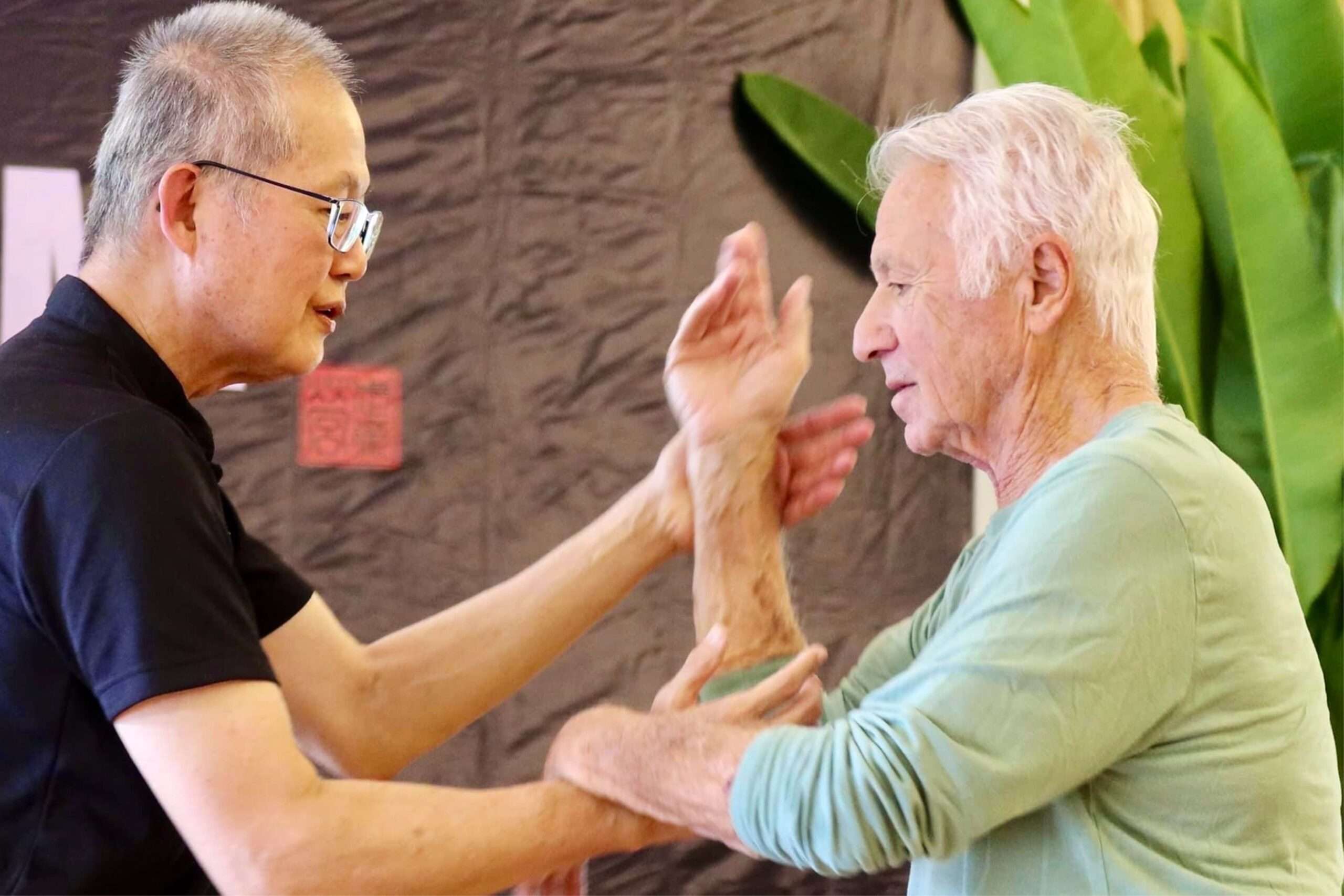 An older teacher tests a participant’s arm structure, both smiling