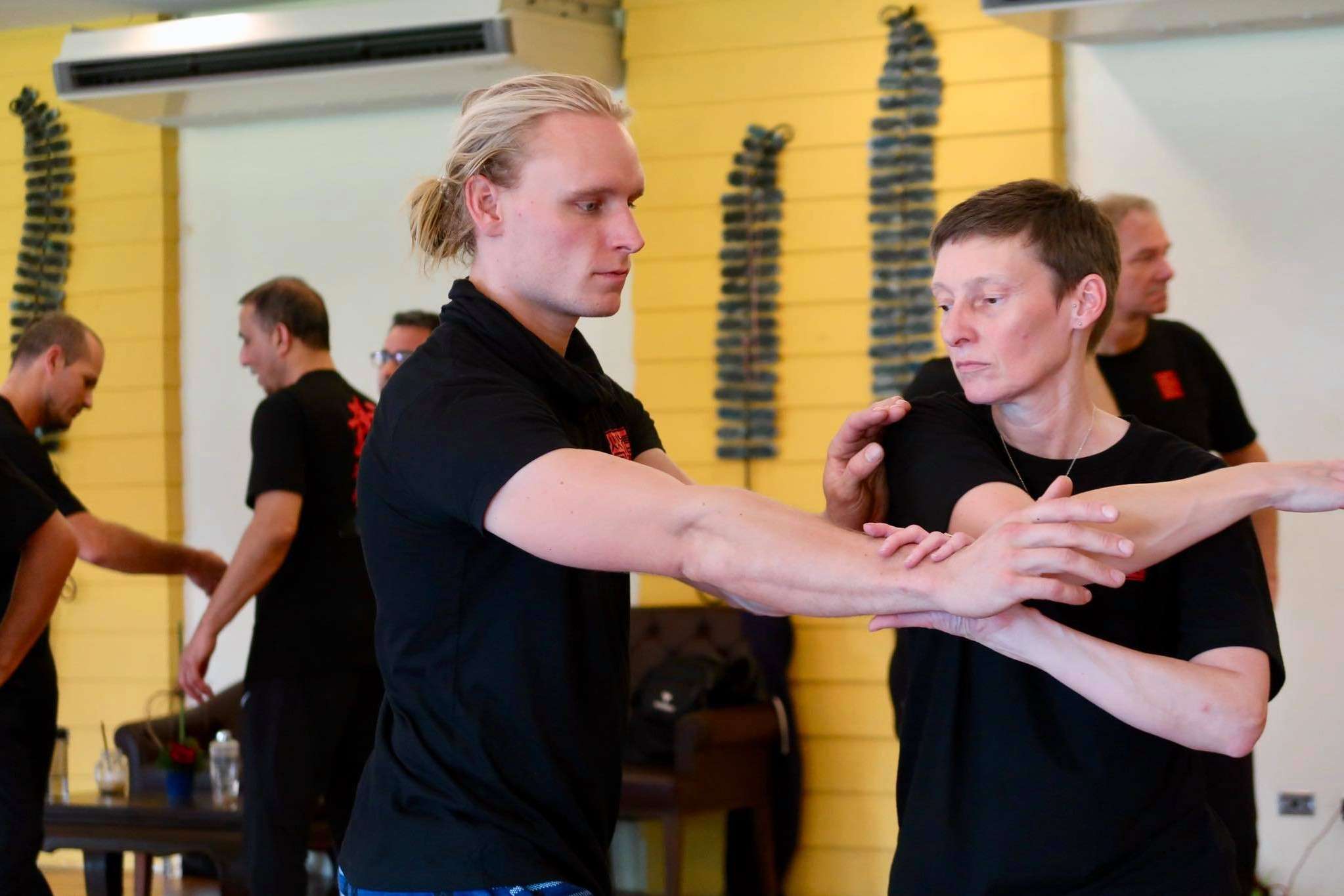 A man with his hair tied back presses his forearms against a partner’s in a partner drill, both concentrating