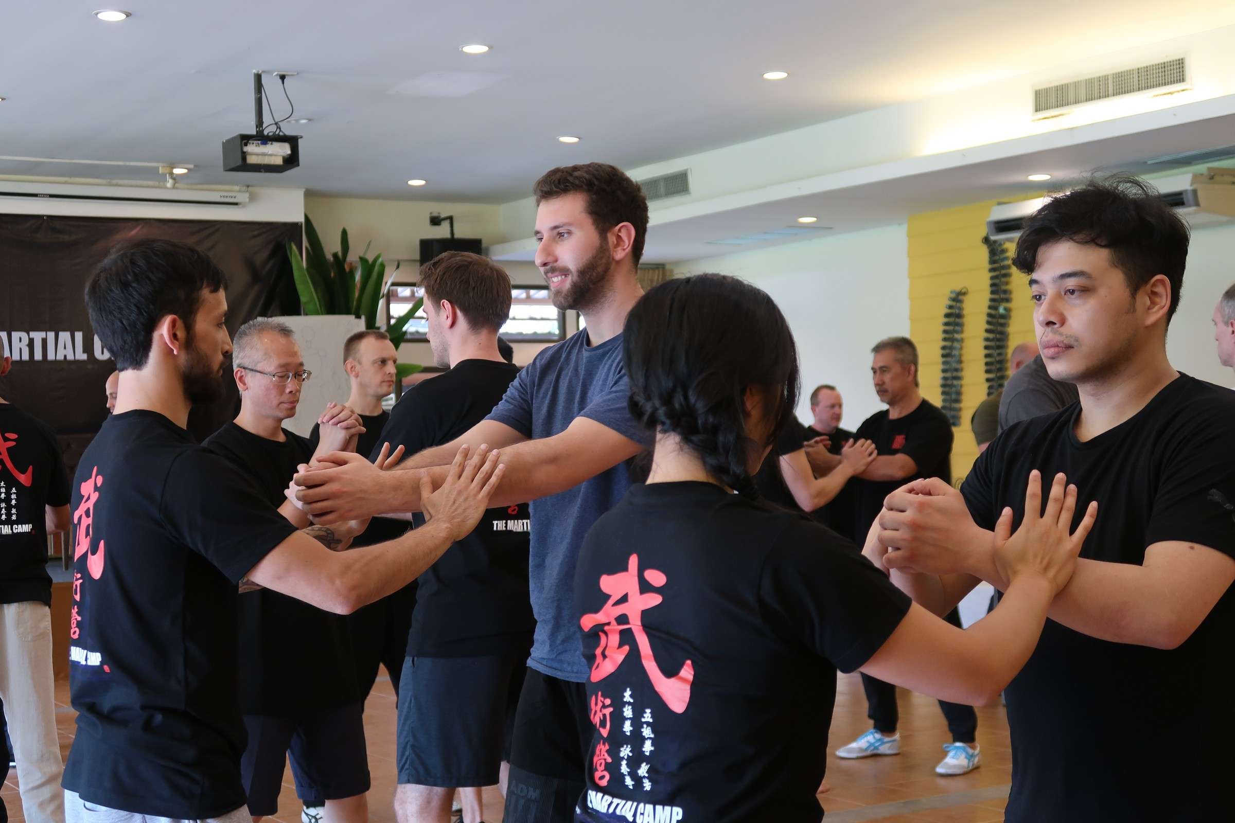 Participants in Martial Camp T-shirts practise a partner drill in pairs across the training hall