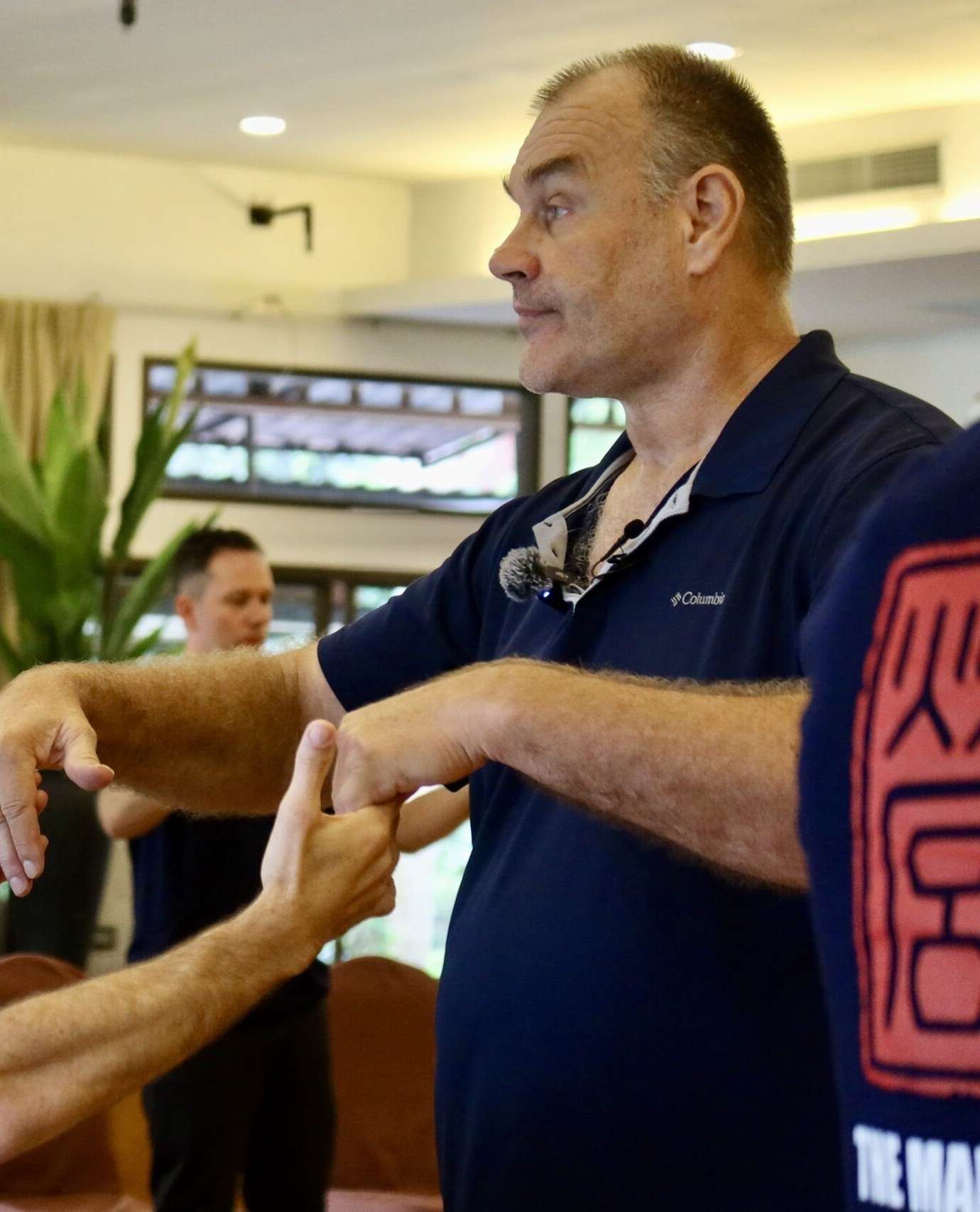 A teacher in a navy polo shirt works arm to arm with a participant, testing his structure